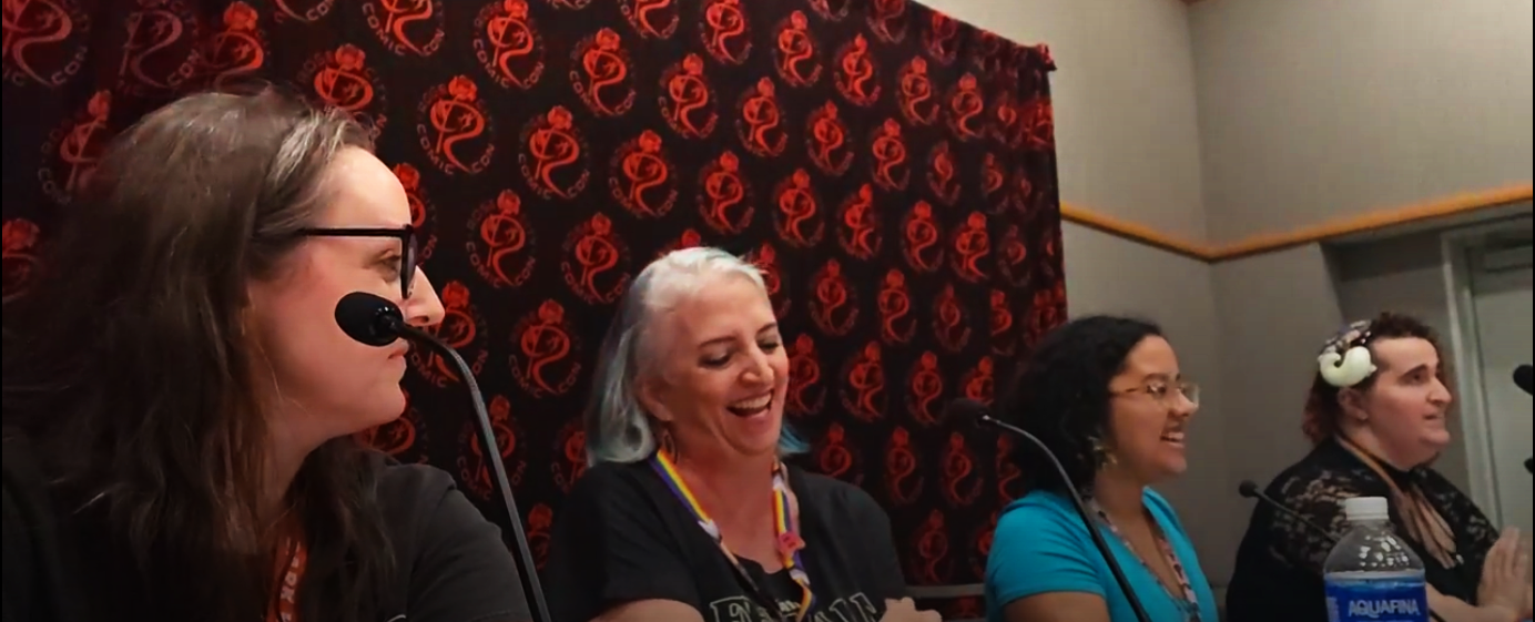 Four people sitting behind microphones presenting a panel