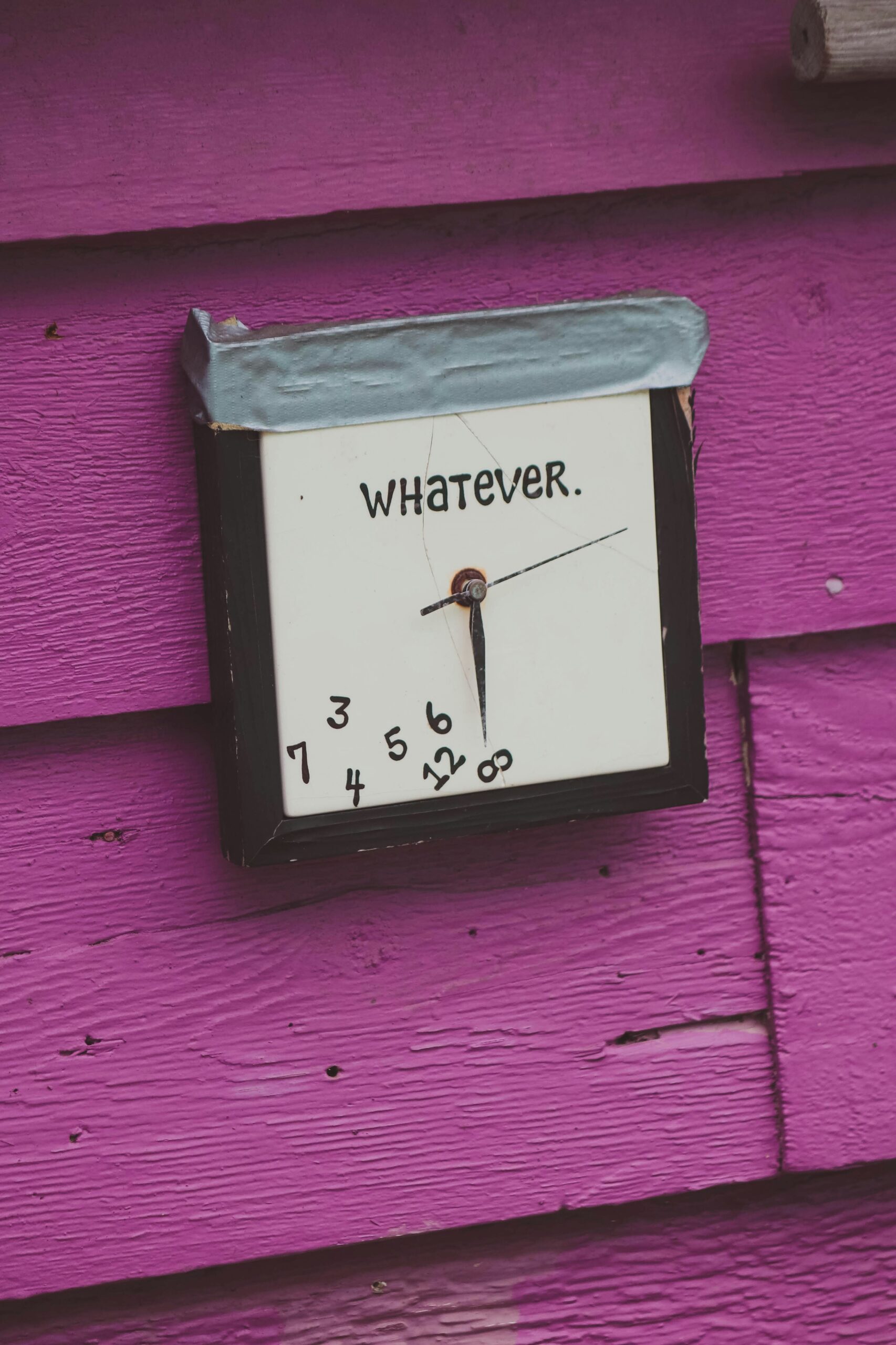 julian-gentile-broken-clock A white clock that all the numbers have fallen off and reads "whatever" hung on a purple wall